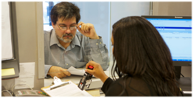 Prestation de services à TJSO. Un homme ajuste ses lunettes en regardant une femme estampiller ses formulaires.